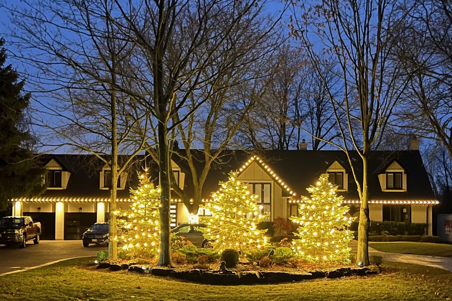 Home with lit trees and warm roofline lighting