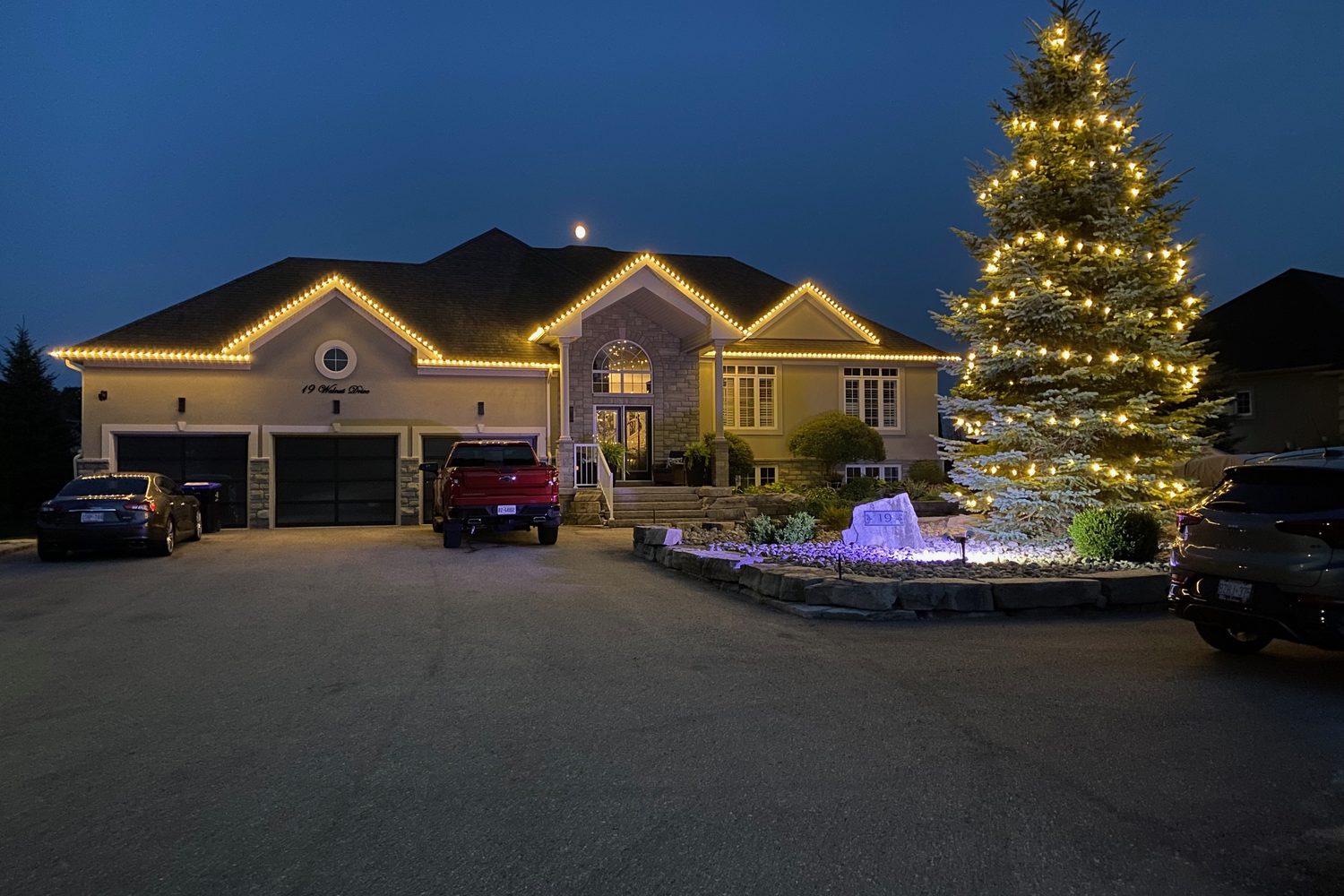 Home with warm-white roofline lighting and a lit evergreen